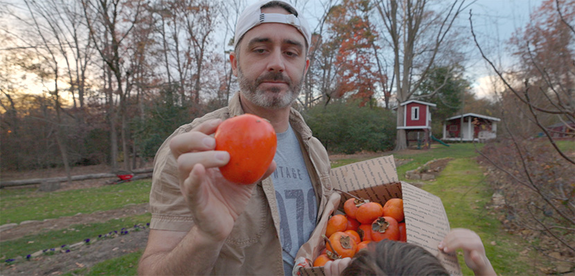 Are persimmons good for you? A man hold a box of persimmons with one held up closer to the camera. 